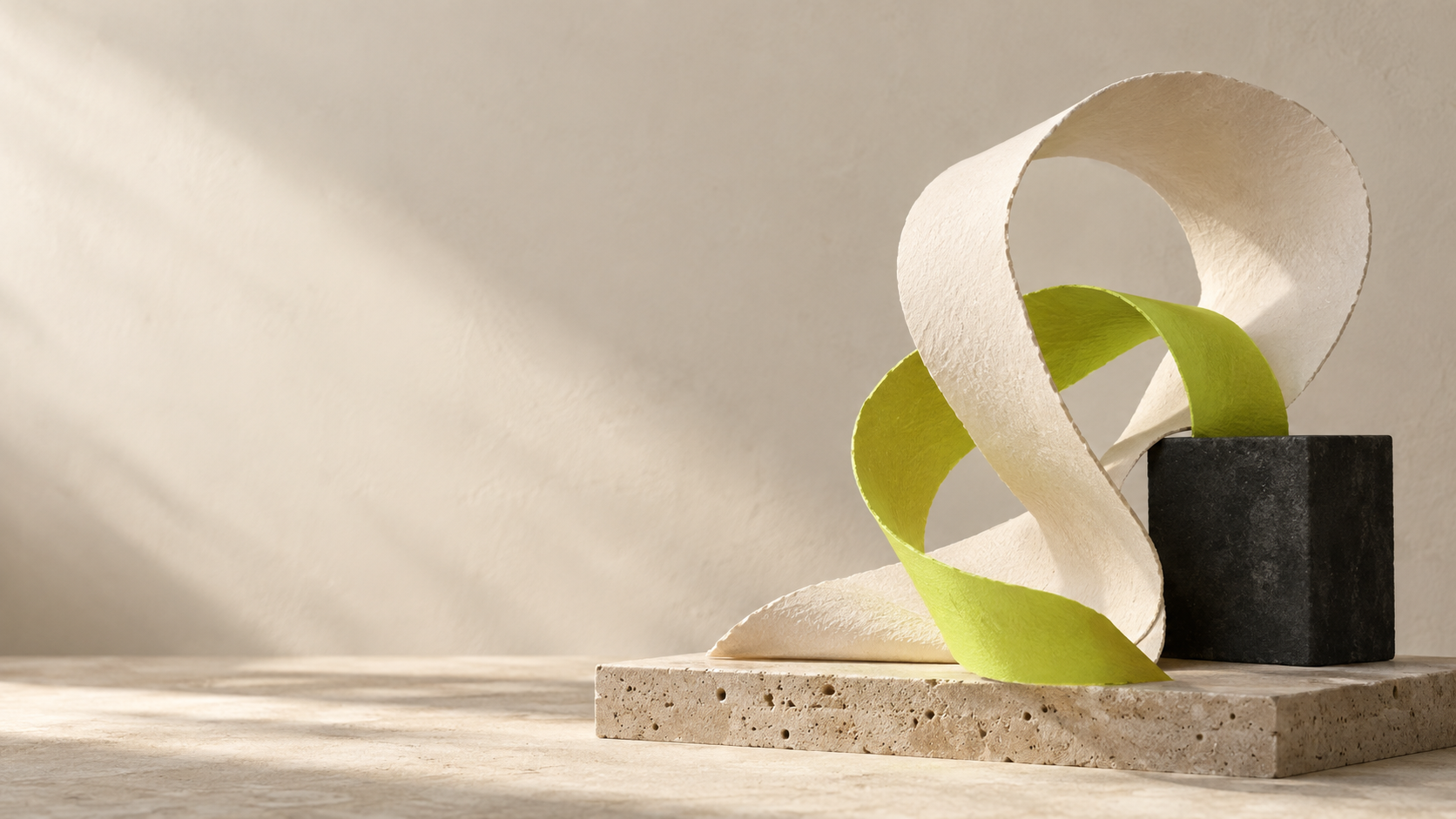 An ivory paper sculpture with a lime ribbon taking shape on a sunlit stone plinth